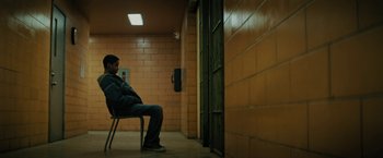 Movie still from “Kin” (2018), directed by Josh Baker – A man sitting on a chair in a jail cell; Wide shot, High angle