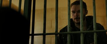 Movie still from “Kin” (2018), directed by Josh Baker – A man standing behind bars in a jail cell; Close Up shot, Low angle