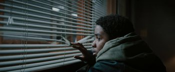 Movie still from “Kin” (2018), directed by Josh Baker – A young man looking out of a window through blinds; Close Up shot, Low angle