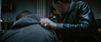Movie still from “Kin” (2018), directed by Josh Baker – A man is helping another man put on a jacket; Medium shot, Over the shoulder angle