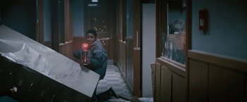 Movie still from “Kin” (2018), directed by Josh Baker – A young boy holding a bottle of soda in a hallway; Medium shot, Low angle