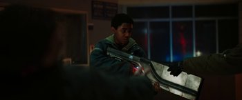 Movie still from “Kin” (2018), directed by Josh Baker – A young man holding a gun in a room; Medium shot, Over the shoulder angle