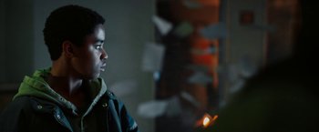 Movie still from “Kin” (2018), directed by Josh Baker – A young man standing next to a candle in a room; Close Up shot, Over the shoulder angle