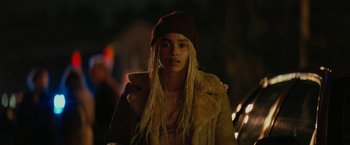 Movie still from “Kin” (2018), directed by Josh Baker – A woman with long blonde hair wearing a hat and a fur coat; Close Up shot, Over the shoulder angle