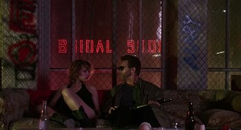 Movie still from “Kindergarten Cop” (1990), directed by Ivan Reitman – A man and a woman sitting in front of a bridal shop sign; Wide shot, Low angle