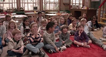 Movie still from “Kindergarten Cop” (1990), directed by Ivan Reitman – A group of children sitting on the floor of a classroom; Wide shot, High angle