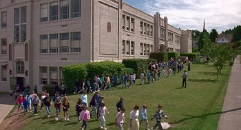 Movie still from “Kindergarten Cop” (1990), directed by Ivan Reitman – A large group of people walking on the grass outside of a building; Extreme Wide shot, High angle