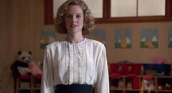 Movie still from “Kindergarten Cop” (1990), directed by Ivan Reitman – A woman standing in front of a wall with pictures on the wall; Medium shot, Low angle