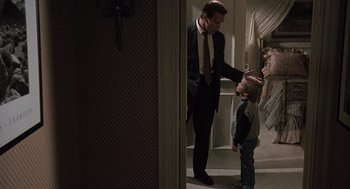 Movie still from “Kindergarten Cop” (1990), directed by Ivan Reitman – A man in a suit and a tie standing next to a young boy; Medium shot, Over the shoulder angle