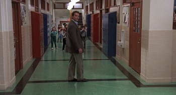 Movie still from “Kindergarten Cop” (1990), directed by Ivan Reitman – A man in a suit standing in a school hallway; Wide shot, Over the shoulder angle