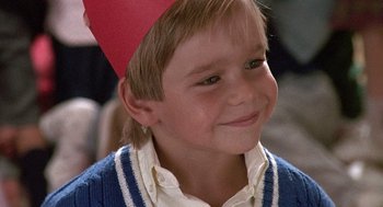 Movie still from “Kindergarten Cop” (1990), directed by Ivan Reitman – A young boy wearing a red paper hat and a blue sweater; Close Up shot, High angle