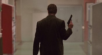 Movie still from “Kindergarten Cop” (1990), directed by Ivan Reitman – A man holding a gun while standing in a room; Wide shot, Low angle