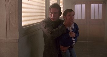 Movie still from “Kindergarten Cop” (1990), directed by Ivan Reitman – A man and a boy are standing in a room together; Medium shot, Over the shoulder angle