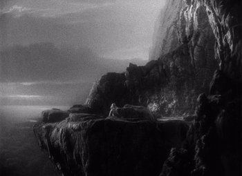 Movie still from “King Kong” (1933), directed by Merian C. Cooper – A black - and - white photo of a cliff with a person lying on it; Extreme Wide shot, High angle