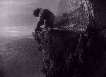 Movie still from “King Kong” (1933), directed by Merian C. Cooper – A black - and - white photo of a man on a cliff; Wide shot, Low angle