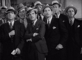 Movie still from “King Kong” (1933), directed by Merian C. Cooper – A black and white photo of a group of men in suits and hats; Medium shot, High angle