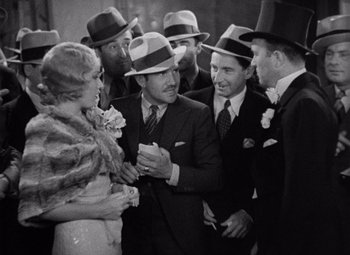 Movie still from “King Kong” (1933), directed by Merian C. Cooper – A group of men standing around a woman in a dress; Medium shot, High angle