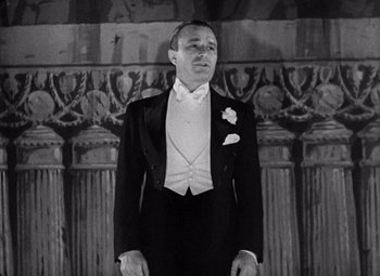 Movie still from “King Kong” (1933), directed by Merian C. Cooper – A man in a tuxedo standing in front of a wall; Medium shot, Low angle