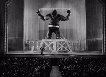 Movie still from “King Kong” (1933), directed by Merian C. Cooper – A man standing on top of a stage with a gorilla on it's back; Extreme Wide shot, Low angle