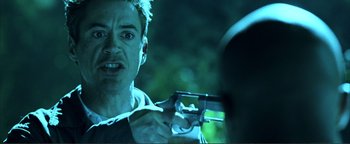 Movie still from “Kiss Kiss Bang Bang” (2005), directed by Shane Black – A person holding a gun in a dark room; Close Up shot, Over the shoulder angle