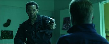 Movie still from “Kiss Kiss Bang Bang” (2005), directed by Shane Black – A man holding a handgun in front of a mirror; Medium shot, Over the shoulder angle