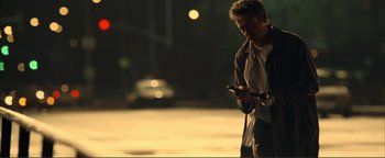 Movie still from “Kiss Kiss Bang Bang” (2005), directed by Shane Black – A man standing on the side of the street looking at his phone; Medium shot, Low angle