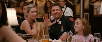 Movie still from “Knight and Day” (2010), directed by James Mangold – A man and a woman sitting at a dinner table waving; Medium shot, Over the shoulder angle