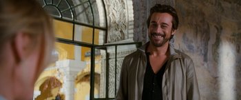 Movie still from “Knight and Day” (2010), directed by James Mangold – A man smiling for the camera while standing next to a building; Close Up shot, Over the shoulder angle