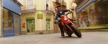 Movie still from “Knight and Day” (2010), directed by James Mangold – A man riding a motorcycle down a street next to a woman; Wide shot, Low angle