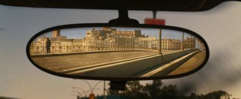 Movie still from “Knight and Day” (2010), directed by James Mangold – A rear view mirror of a car with a city in the background; Extreme Wide shot, Over the shoulder angle