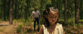 Movie still from “Knock at the Cabin” (2023), directed by M. Night Shyamalan – A young girl standing in front of an older man in the woods; Medium shot, Over the shoulder angle