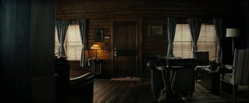 Movie still from “Knock at the Cabin” (2023), directed by M. Night Shyamalan – A living room with a couch , table , lamp and a door; Wide shot, High angle