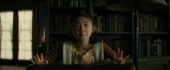 Movie still from “Knock at the Cabin” (2023), directed by M. Night Shyamalan – A young girl sitting in front of a book shelf; Medium shot, High angle
