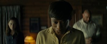Movie still from “Knock at the Cabin” (2023), directed by M. Night Shyamalan – A person with short black hair wearing a yellow shirt; Close Up shot, Over the shoulder angle