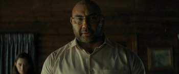 Movie still from “Knock at the Cabin” (2023), directed by M. Night Shyamalan – A man with a beard wearing glasses and a white shirt; Close Up shot, Over the shoulder angle