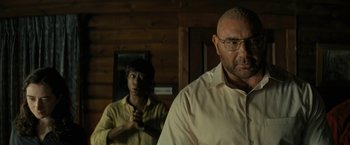 Movie still from “Knock at the Cabin” (2023), directed by M. Night Shyamalan – A man standing next to another man in front of a wooden wall; Medium shot, Over the shoulder angle