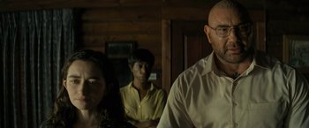 Movie still from “Knock at the Cabin” (2023), directed by M. Night Shyamalan – A man and a woman standing in front of another man in front of another man; Medium shot, Over the shoulder angle