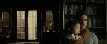 Movie still from “Knock at the Cabin” (2023), directed by M. Night Shyamalan – A woman sitting in front of a window in a living room; Medium shot, Over the shoulder angle