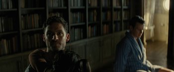 Movie still from “Knock at the Cabin” (2023), directed by M. Night Shyamalan – A man standing in front of bookshelves in a room; Close Up shot, Over the shoulder angle