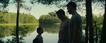 Movie still from “Knock at the Cabin” (2023), directed by M. Night Shyamalan – Three men and a little girl standing by a body of water; Medium shot, Over the shoulder angle