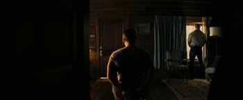 Movie still from “Knock at the Cabin” (2023), directed by M. Night Shyamalan – A man standing in front of a door in a room; Wide shot, Low angle
