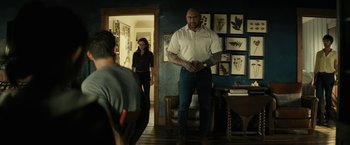 Movie still from “Knock at the Cabin” (2023), directed by M. Night Shyamalan – A man standing in front of a woman in a living room; Medium shot, Over the shoulder angle