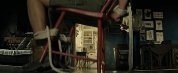 Movie still from “Knock at the Cabin” (2023), directed by M. Night Shyamalan – A person is sitting in a chair with ropes around them; Wide shot, Low angle