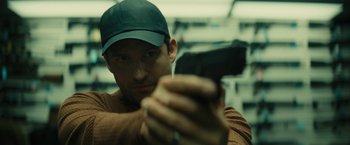 Movie still from “Knock at the Cabin” (2023), directed by M. Night Shyamalan – A man holding a gun while wearing a baseball cap; Close Up shot, Low angle