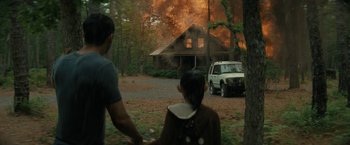 Movie still from “Knock at the Cabin” (2023), directed by M. Night Shyamalan – A man and a child watch a house on fire; Wide shot, Over the shoulder angle