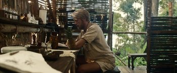 Movie still from “Kon-Tiki” (2012), directed by Espen Sandberg – A man sitting at a table holding a pineapple; Medium shot, Over the shoulder angle