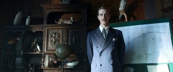 Movie still from “Kon-Tiki” (2012), directed by Espen Sandberg – A man in a suit standing in front of an antique cabinet; Medium shot, Low angle