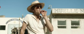 Movie still from “Kon-Tiki” (2012), directed by Espen Sandberg – A man wearing a straw hat and sunglasses eating a piece of food; Medium shot, Low angle