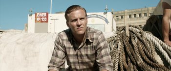 Movie still from “Kon-Tiki” (2012), directed by Espen Sandberg – A man in a plaid shirt sitting next to ropes; Medium shot, Low angle