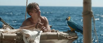 Movie still from “Kon-Tiki” (2012), directed by Espen Sandberg – A man sitting on top of a boat next to a parrot; Medium shot, Low angle